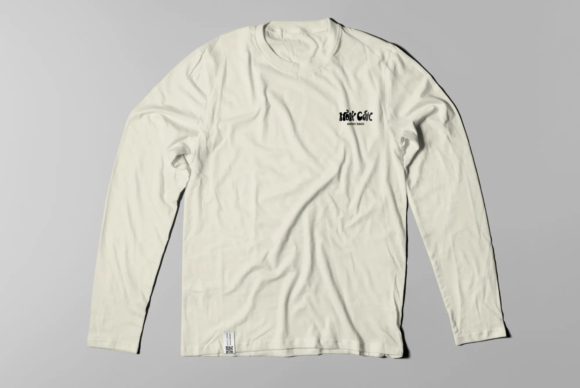 T-shirt blanc à manches longues avec un logo noir "HOK COK" et le texte "Gourmet Burger" sur la poitrine, posé sur un fond gris.
