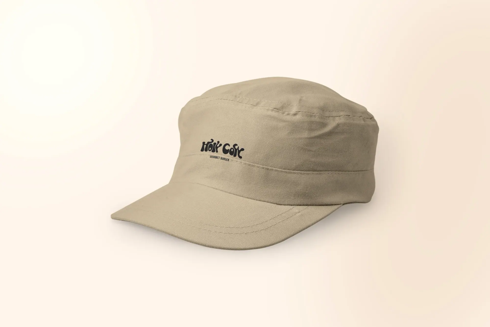 Casquette beige avec le logo 'Holy Code, Gourmet Burger' en noir, posée sur un fond beige clair.