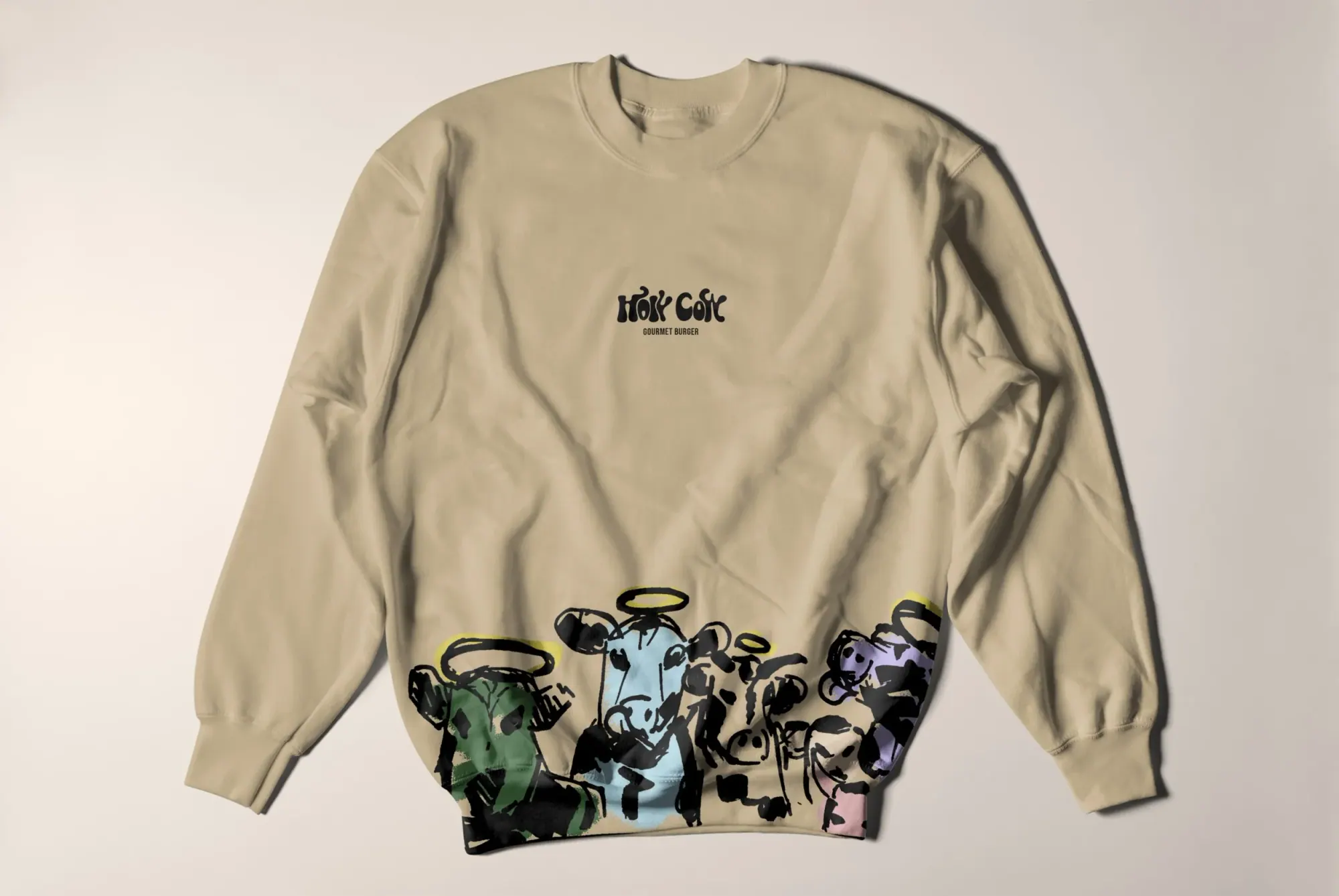 Sweatshirt beige avec un dessin de vaches stylisées au bas, portant des halo et avec le texte 'Hok Cek' et 'Gourmet Burger' au centre.