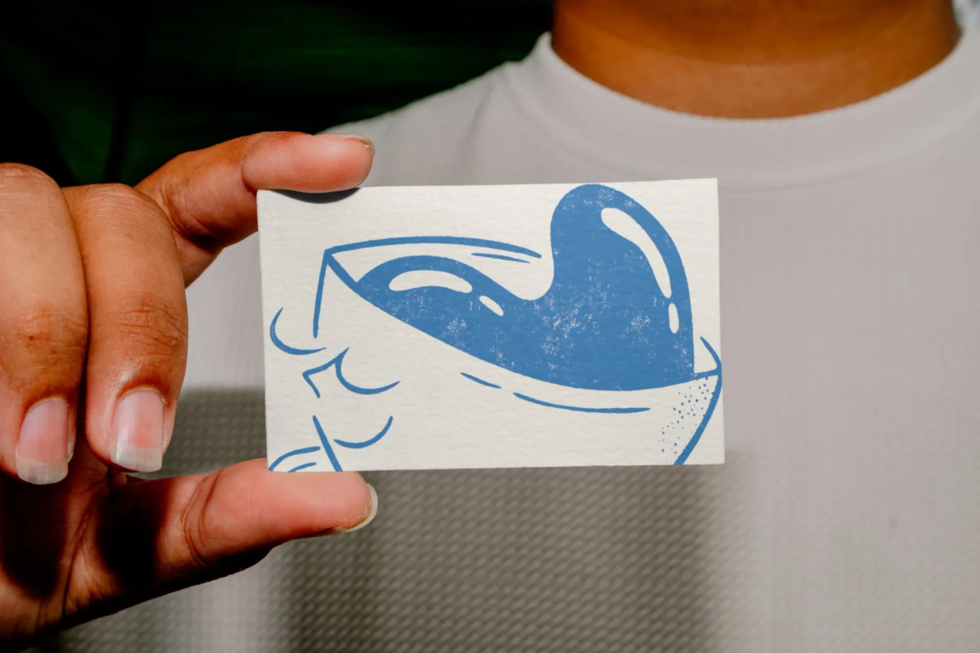 Une personne tient une petite carte avec une illustration bleue d'une paille dans un verre. La personne porte un haut blanc et a la peau teintée.