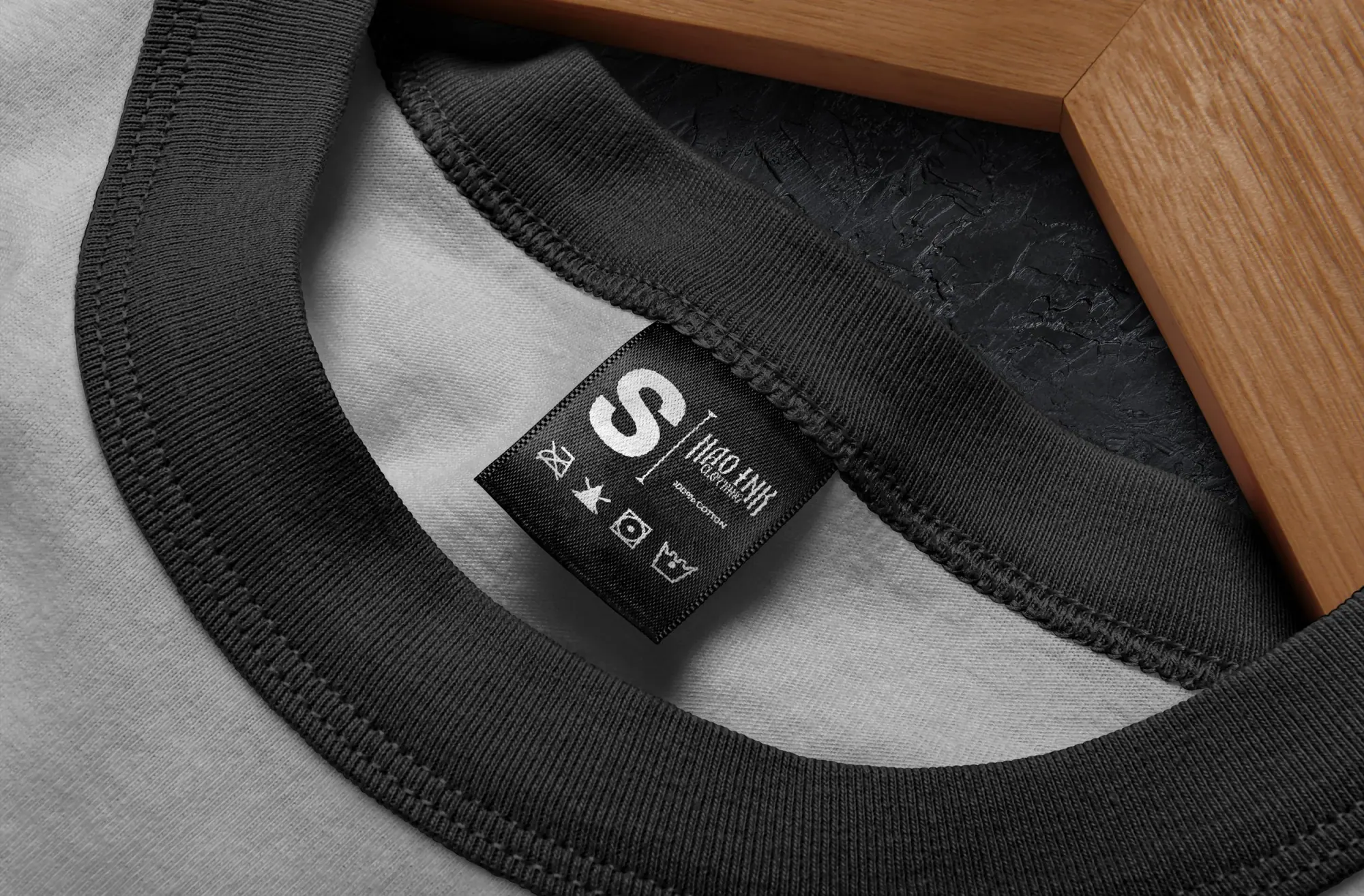 Étiquette de vêtement noir avec taille S, au centre d'un col de t-shirt gris, posé sur un fond en bois et noir.